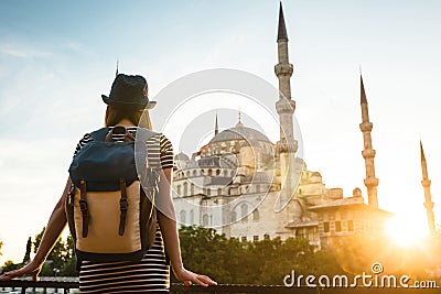 Young beautiful girl traveler in a hat with a backpack looking at a blue mosque - a famous tourist attraction of Stock Photo