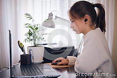 Young beautiful girl works at a laptop, holding a hand on a computer mouse at home at a work table in a bright room. Stock Photo