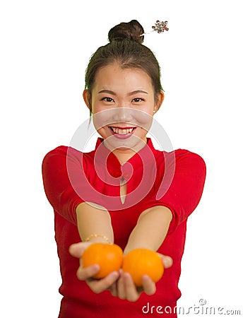 Young beautiful and happy Asian woman in traditional Chinese New Year red dress holding orange fruit as symbol of prosperity Stock Photo