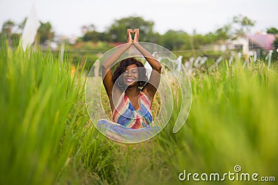 Young beautiful and happy black African American woman sitting at rive field outdoors practicing yoga relaxation and meditation Stock Photo