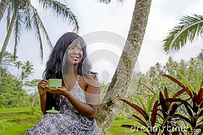 Young beautiful and happy black afro American tourist woman drinking coffee or tea visiting jungle plantation in Thailand or Vietn Stock Photo