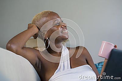 Young beautiful happy black afro American woman smiling working on laptop computer at home relaxed on sofa couch in internet onlin Stock Photo