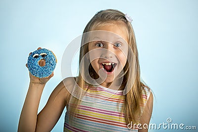 Young beautiful happy and excited blond girl 8 or 9 years old holding donut desert on her hand looking spastic and cheerful in sug Stock Photo