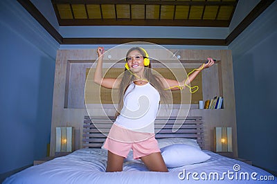 Young beautiful and happy student woman Asian Latin ethnicity mixed listening to music with headphones in bed singing and dancing Stock Photo