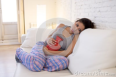 Young beautiful hispanic woman holding hot water bottle against belly suffering menstrual period pain Stock Photo