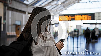 Young beautiful hispanic woman looking at train schedule on smartphone at train station Stock Photo