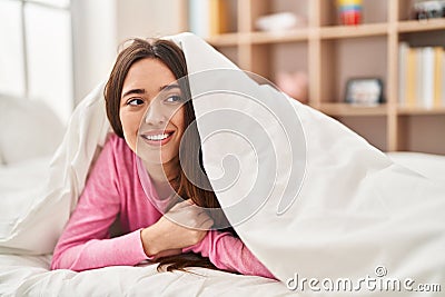 Young beautiful hispanic woman lying on bed covering with bedsheet at bedroom Stock Photo