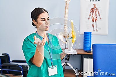 Young beautiful hispanic woman physiotherapist holding anatomical model of knee at rehab clinic Stock Photo