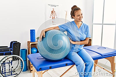 Young beautiful hispanic woman physiotherapist smiling confident holding fit ball at rehab clinic Stock Photo