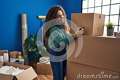 Young beautiful hispanic woman smiling confident writing kitchen word on package at new home Stock Photo
