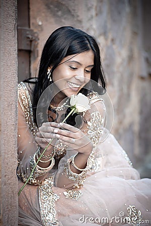 Young beautiful Indian Woman sitting against stone wall outdoors Stock Photo