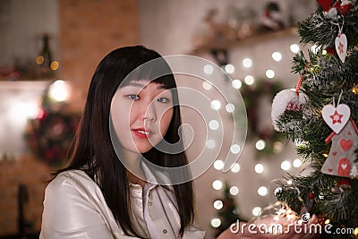 A young, beautiful Korean Asian woman holds a lighted festive garland in her cozy home with dreams of positive emotions Stock Photo