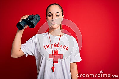 Young beautiful lifeguard woman wearing t-shirt with red cross and whistle using binoculars with a confident expression on smart Editorial Stock Photo