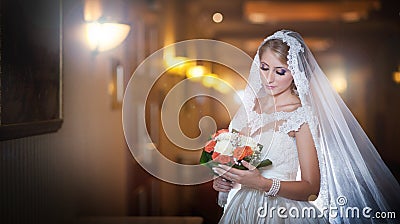 Young beautiful luxurious woman in wedding dress posing in luxurious interior. Bride with long veil holding her wedding bouquet Stock Photo