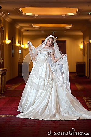 Young beautiful luxurious woman in wedding dress posing in luxurious interior. Gorgeous elegant bride with long veil. Full length Stock Photo