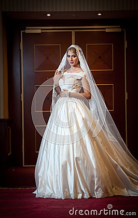 Young beautiful luxurious woman in wedding dress posing in luxurious interior. Gorgeous elegant bride with long veil. Full length Stock Photo