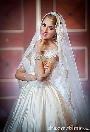Young beautiful luxurious woman in wedding dress posing in luxurious interior. Gorgeous elegant bride with long veil. Full length Stock Photo