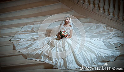 Young beautiful luxurious woman in wedding dress sitting on stair steps in semi-darkness. Bride with huge wedding dress Stock Photo