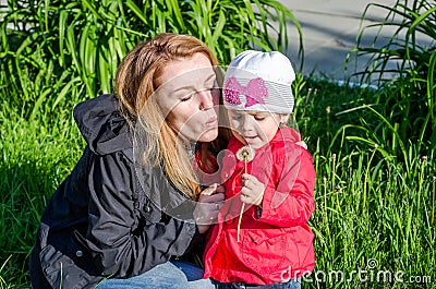 Young beautiful mother with adorable little daughter Baby girl with long hair Europeans in a meadow with grass and flowers Stock Photo