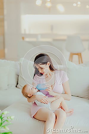 Young beautiful mother bottle feeding her little son at home Stock Photo
