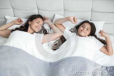 Young beautiful mother and her cute teen daughter just woke up together in bed both stretchin Stock Photo