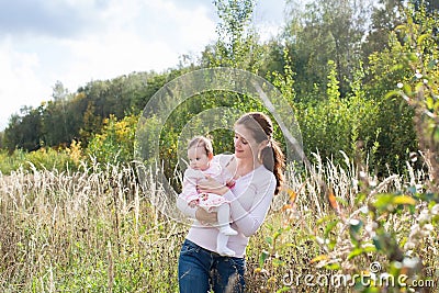 Young beautiful mother holding a baby girl wearing a pink dress in a meadow Stock Photo