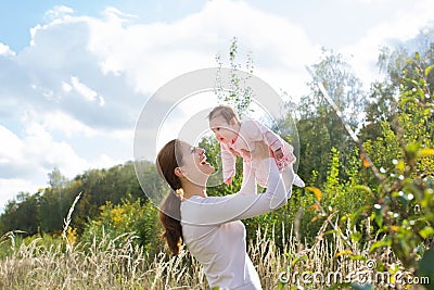 Young beautiful mother holding a baby girl wearing a pink dress in a meadow Stock Photo