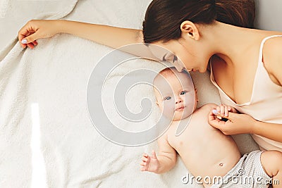 Young beautiful mother lies the baby on the bed, gently kisses, sleeping together Stock Photo