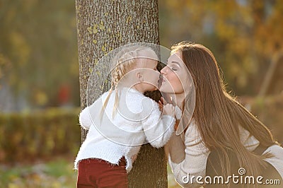 A young beautiful mother in a sweater and her cute daughter are having fun on a walk in the autumn Park. Mom plays with Stock Photo