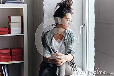 Young beautiful pensive woman with dark curly hair sitting on window sill in audience of university thoughtfully looking Stock Photo