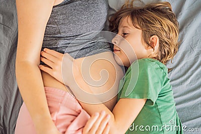 Young beautiful pregnant woman and eldest son. The cute boy leaned his ear against his mother& x27;s belly. Expecting a Stock Photo