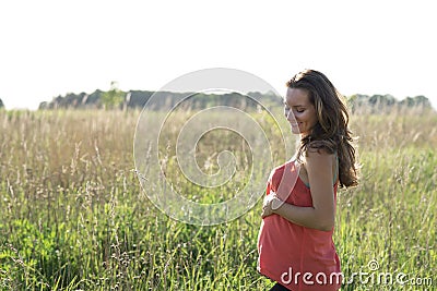 Young beautiful pregnant woman holding tummy smiling, in red a light summer dress, happy on meadow the grass Stock Photo