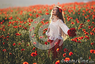 Young beautiful woman walking and dancing through a poppy field at sunset Stock Photo