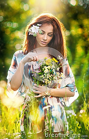 Young beautiful red hair woman holding a wild flowers bouquet in a sunny day. Portrait of attractive long hair female with flowers Stock Photo