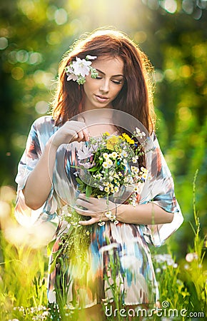 Young beautiful red hair woman holding a wild flowers bouquet in a sunny day. Portrait of attractive long hair female with flowers Stock Photo