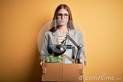 Young beautiful redhead businesswoman fired holding carboard box over yellow background with a confident expression on smart face Stock Photo