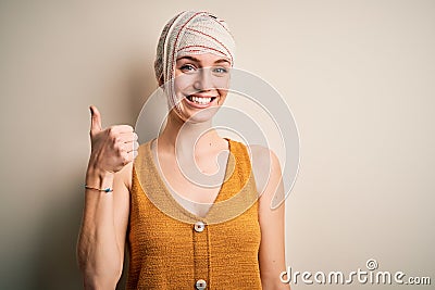 Young beautiful redhead woman injured for accident wearing bandage on head doing happy thumbs up gesture with hand Stock Photo