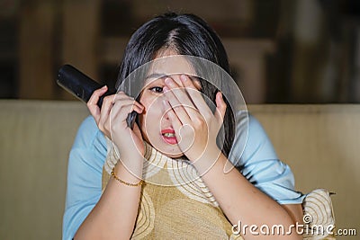 Young beautiful and scared Asian Chinese teenager woman in fear watching horror scary movie at home sofa couch eating popcorn bowl Stock Photo