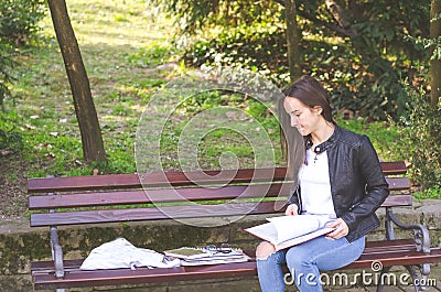 Young beautiful school or college girl with glasses sitting on the bench in the park reading the books and study for exam Stock Photo