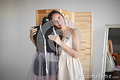 Young beautiful seamstress hugs a manikin at her workplace Stock Photo