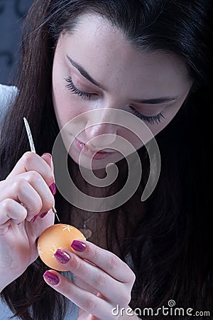 Young beautiful sexy german woman with dark hair paints a yellow Easter egg according to Sorbian tradition with a needle head and Stock Photo