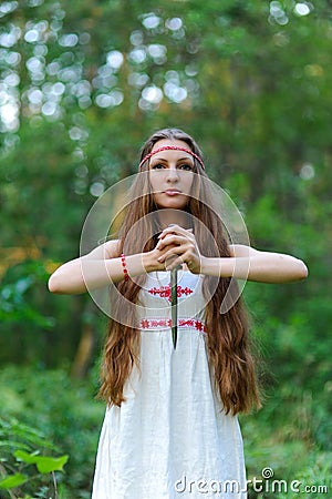 A young beautiful Slavic girl with long hair and Slavic ethnic dress stands in a summer forest with a ritual dagger in her hands Stock Photo