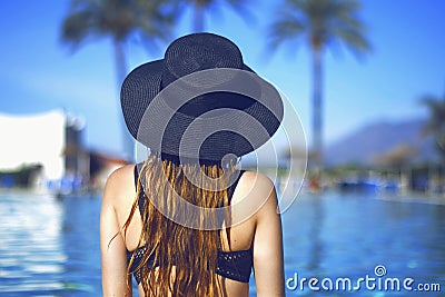 Young beautiful smile girl in black fashion hat, red lips and long hair, posing near pool beackground of palms. Stock Photo