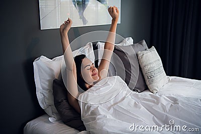 Young beautiful smiling and brunette woman lying in bed trying to wake up early morning stretching hands after sleep Stock Photo