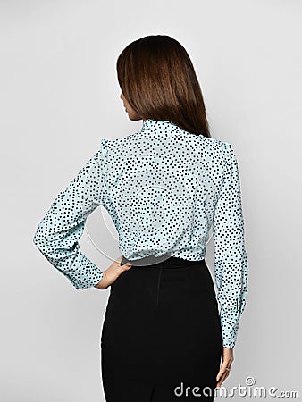 Young beautiful smiling brunette woman in stylish white dotted shirt and black skirt backside view from behind Stock Photo