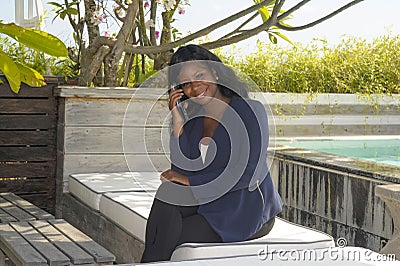 Young beautiful and successful black Afro American woman on her 30s wearing formal business clothes sitting at pool resort working Stock Photo