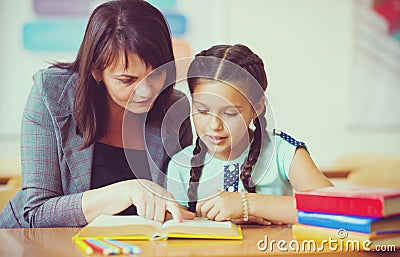 Young beautiful teacher with schoolgirl reading book in the classroom Stock Photo