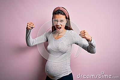Young beautiful teenager girl pregnant expecting baby over isolated pink background angry and mad raising fists frustrated and Stock Photo