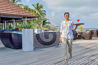 Young beautiful waitress walking with the cocktail on the tray at the tropical`s island bar Editorial Stock Photo