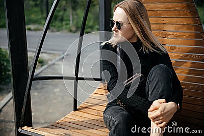 Young beautiful white girl is sitting on a park bench.Cute female lifestyle, portrait with soft focus.Thoughtful stylish Stock Photo